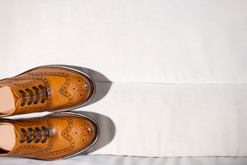 Footwear Concepts. Closeup of Full Broggued Tan Leather Oxfords Shoes Ion Pale Color Sofa. Placed Together.