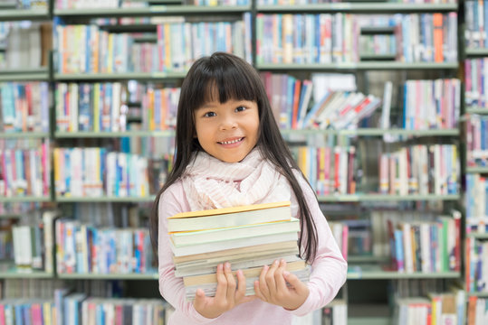 child girl holding a stack of books in the library