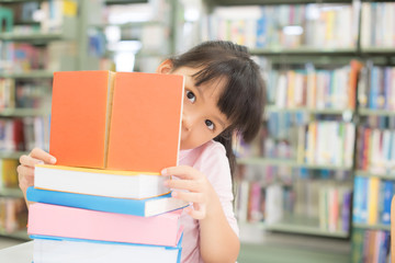 The girl reads in the library. She hides behind the book.