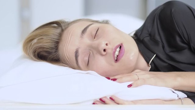 Woman can't sleep because noisy in home and turns from side to side puts a pillow on his head in bed resting attractive female lying tired beautiful morning dream relax slow motion