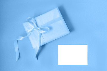 Gift box with silk ribbon in trendy blue color and empty isolated label. Flat lay. Holiday gift concept. Color of the year 2020 concept. Copy space.