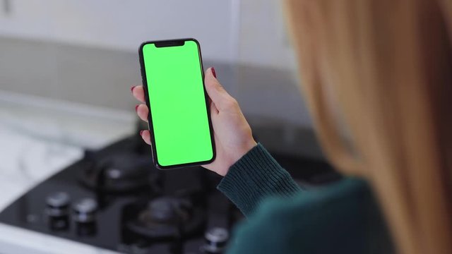 Young hands woman holding use smartphone with vertical green screen mobile phone background kitchen technology information communication device business girl cellphone display slow motion