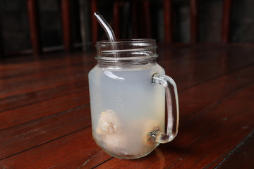 A glass of eco-friendly ice lychee  drink with glass straw with wood background