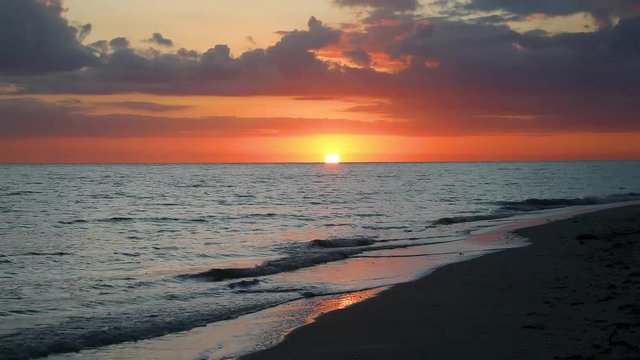 The sky is painted with beautiful color at sunset over waves breaking on a sandy Gulf of Mexico vacation beach on Sanibel Island, Florida in this looping video