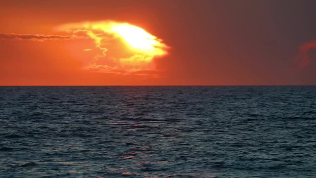 The sunshine is bright and dramatic through a colorful break in the clouds low on the horizon near sunset over the ocean waves of the Gulf of Mexico in this seamless background video loop