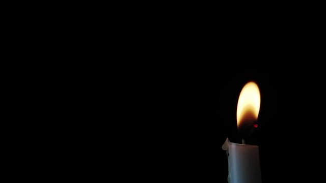 A single candle burns its flame, flickering in the darkness in a looping video with lots of copy space