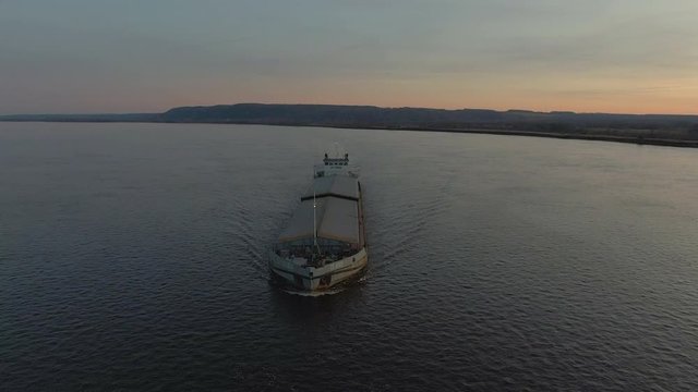 Freight ship floating on sea on sunset landscape. Aerial front view cargo ship with freight sailing in river on forest and sunset landscape. Drone view from above.
