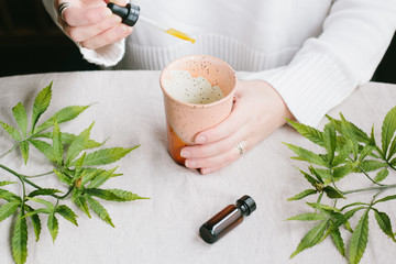 Woman's hands, glass bottles with CBD oil, THC tincture and hemp leaves. Flat lay, minimalism....