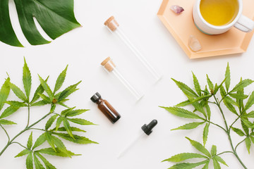 Glass bottles with CBD oil, THC tincture and hemp leaves on a white background. Flat lay,...
