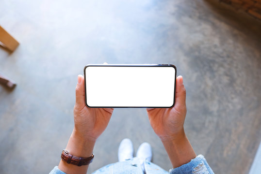Top view mockup image of a woman standing and holding black mobile phone with blank white screen