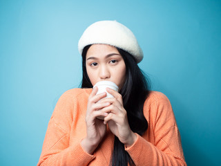 Happy Asian woman wearing sweater and drinking coffee take away on blue background.