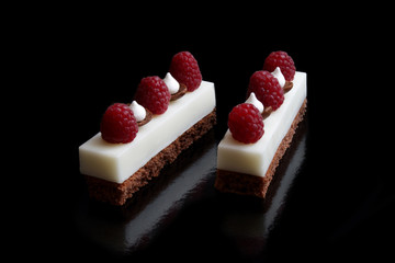 Two white mascarpone cheese mousse sheet cake slices with raspberries and meringues on brownie base