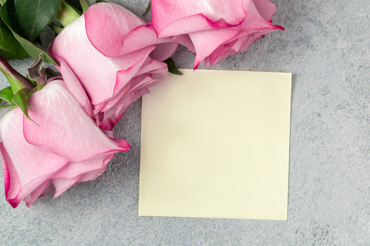 Flower arrangement - a bouquet of pink roses and an empty sheet for a note on a grey concrete surface