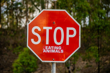 Vertical image of a tradional red traffic warning sign which has been cleverly vandalised with a sticker to read 'STOP Eating Animals'.  Clever social environment, vegentarian and vegan message