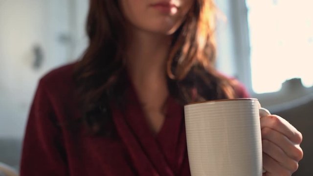 Woman in robe  hods hot drink as steam rises in slow motion