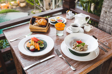 Breakfast with balinese fruit plate, basket with croissants and fruit salad on wooden table