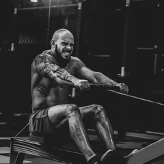 Fit athletic young man doing seated cable row in gym, dramatic black and white image