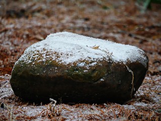 Big rock in the garden partially covered with snow dusting and ice on the ground