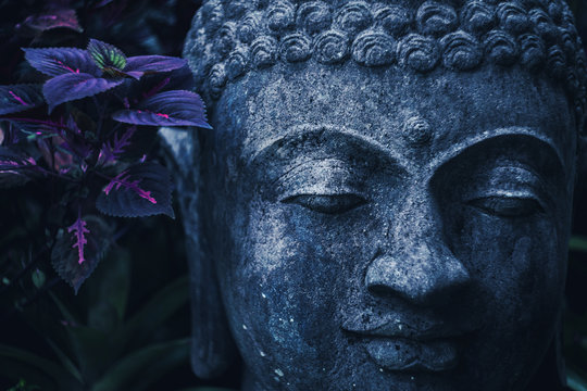 Stone Buddha face close-up in trend blue color toning. Handmade carved Buddha statue in balinese garden as decoration.