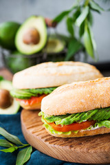 Homemade vegetable sandwich with cream cheese, fresh avocado and tomatoes on a wooden table. Vertical photo