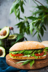 Homemade vegetable sandwich with cream cheese, fresh avocado and tomatoes on a wooden table. Vertical photo. Selective focus.
