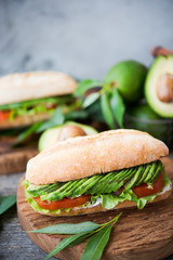 Homemade vegetable sandwich with cream cheese, fresh avocado and tomatoes on a wooden table. Vertical photo. Selective focus.