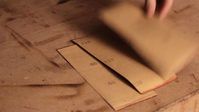 Laying down different types of sandpaper with different levels of grit face down on a wooden surface 