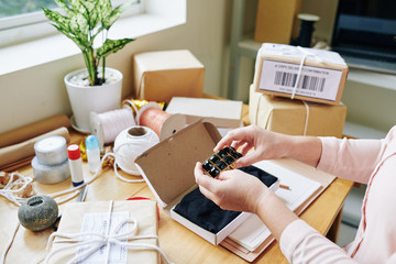 Hands of woman packing handmade jewelry in small box and preparing it for delivery to customers