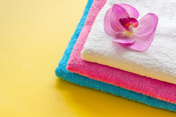 Obraz na płótnie Canvas Clean towels - stack of laundred linen with orchid flower - on yellow background copy space