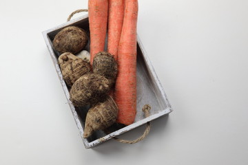 Carrots and Yams in a wooden tray on wooden white background with copy space.