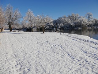 Fototapeta na wymiar Beautiful tranquil view of fresh white snow covering the ground by the pond