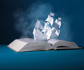 Sailing paper ship created from pages. Ship over an open book. Allegory of interesting contents of...