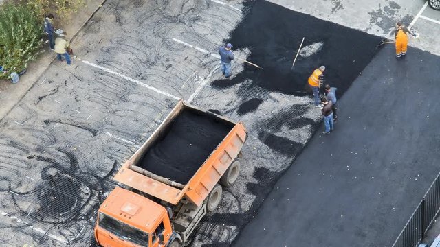 Time lapse of team of workers paving hot asphalt on a parking place . Small steamroller. Road construction workers with shovels in protective uniforms. Aerial, top view