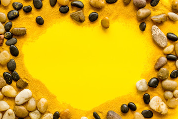 Sea rest, summer vacation concept. Stones and sand on yellow background top-down frame copy space