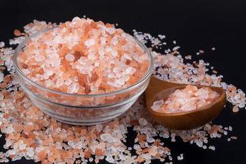 Himalayan pink rock salt in bowl on black background with wooden spoon