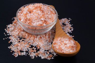 Fototapeta na wymiar Himalayan pink rock salt in bowl with wooden spoon on black table close up