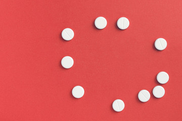 Round pills scattered on a red background. Top view, copy space. Pharmacy concept