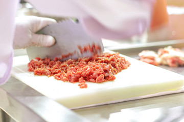Chef is chopping the raw pork on cutting board with  knife to cook in the kitchen, minced pork