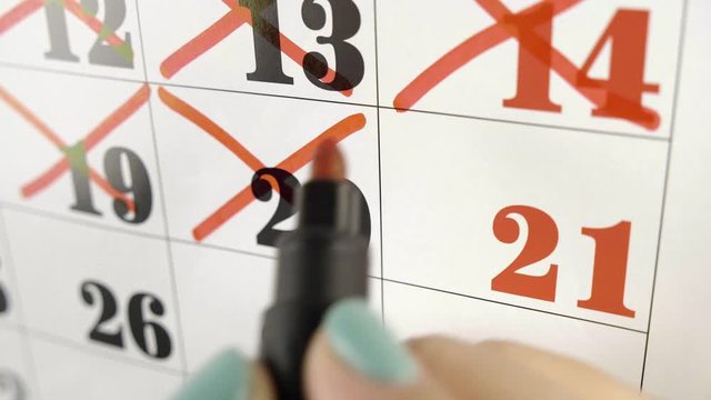 Female hand crosses with red marker the calendar day 21. Slow motion shot. Close up