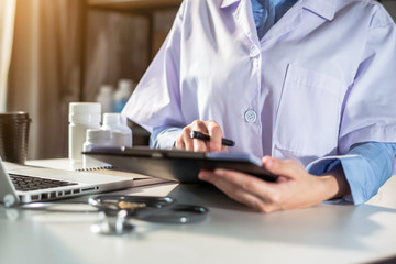 Doctor working on laptop computer, writing prescription clipboard with record information paper folders on desk in clinic, Healthcare and medical concept. Focus on stethoscope.