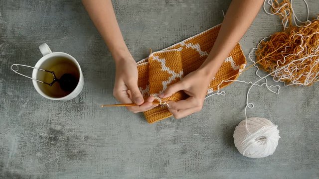 adult girls hands crocheting with orange and white cotton thread on stone table background, top view close-up full HD stock video footage in real-time