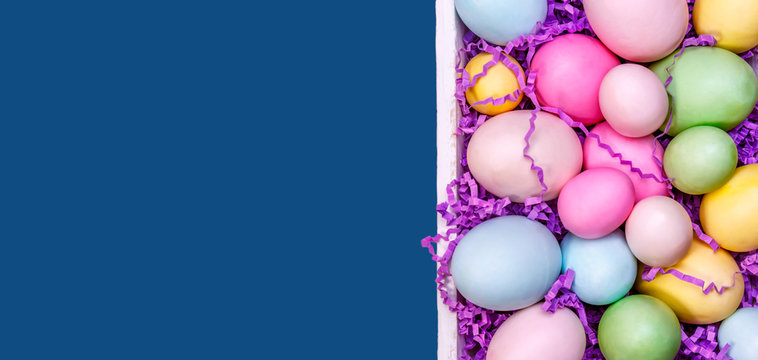 Multicolor eggs in a white tray. Creative Easter concept. Modern solid classic blue background. Horizontal, banner format