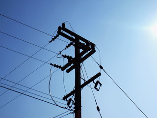 Silhouettes high-voltage wires on a pole. On the blue sky background and copy space.