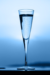 Glass of prosecco at a wooden pier at sunset. Luxury resort vacation concept. Festive relax getaway background toned on blue. Vertical