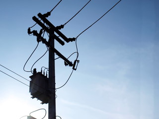 Silhouettes of power transformers and high-voltage wires on a pole. On the blue sky background and copy space.