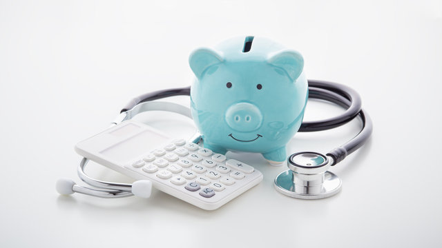 Piggy bank with stethoscope and calculator on white table