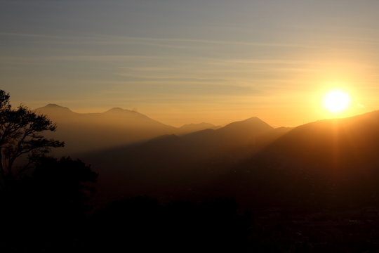 evocative image of sunset with silhouette of mountains in the background  and tree in the foreground