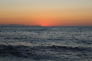 the sun setting behind the promontory with the sea in the foreground