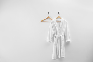 Soft comfortable bathrobe hanging on white wall, space for text