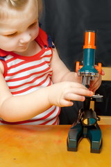 A little girl is studying a children's toy microscope.